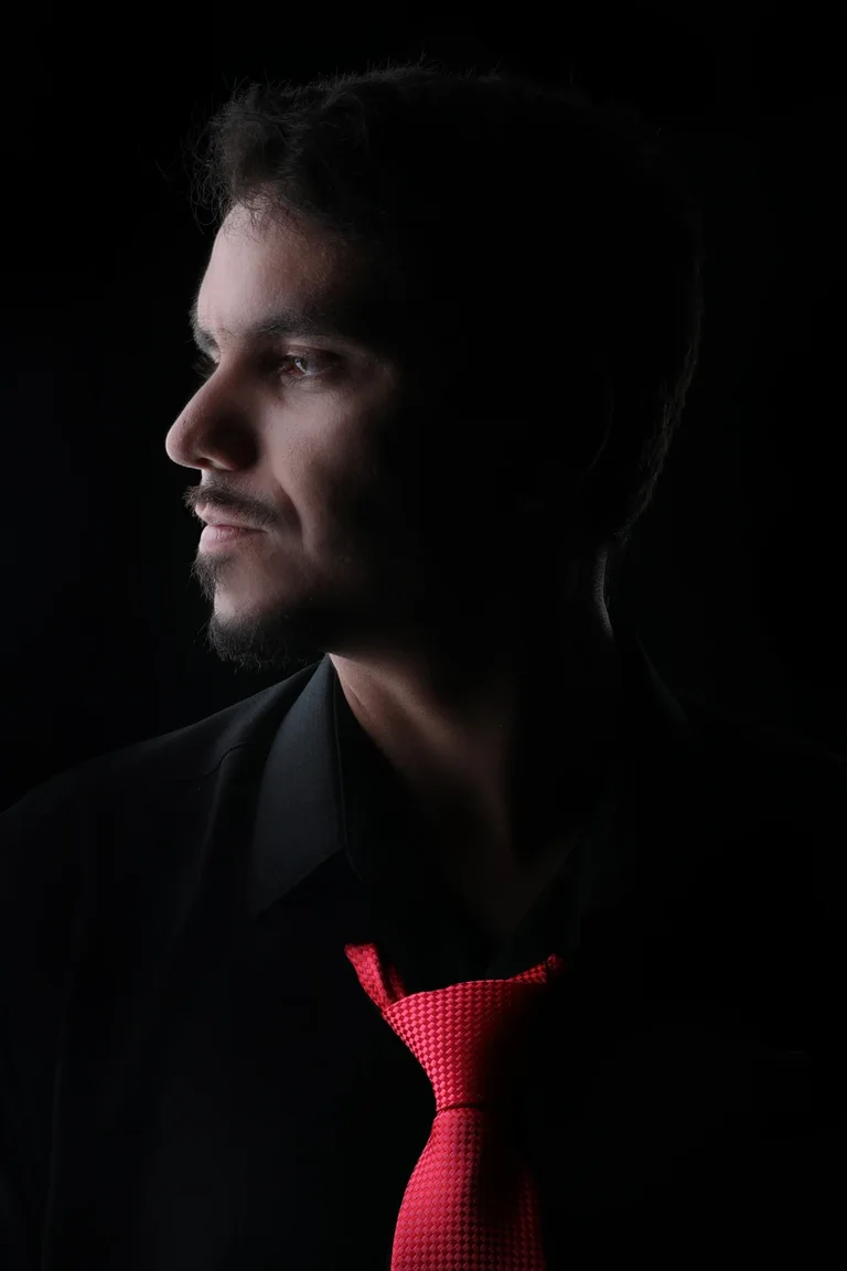 Headshot of Andrés wearing a black shirt and red tie against a black background